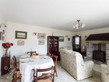 A living room with a dining table set with plates and glasses near a fireplace with floral upholstered sofas at Grazeland Cottage in Bridport