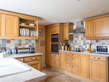 A kitchen with wooden cabinets tiled backsplash and appliances at Grazeland Cottage in Bridport