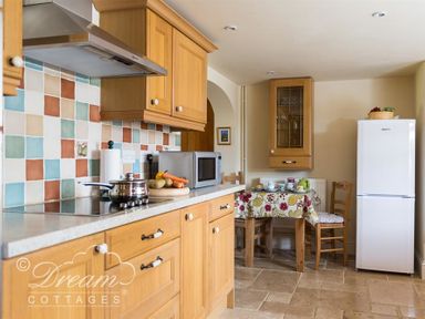 A kitchen with wooden cabinets tiled backsplash stove microwave dining table and white refrigerator at Grazeland Cottage in Bridport