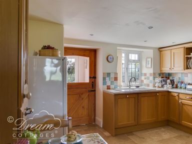 A kitchen with wooden cabinets a white refrigerator a wooden door and a sink under a window at Grazeland Cottage in Bridport