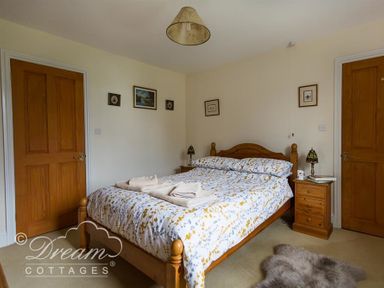 A bedroom with a wooden bed and bedside tables with lamps and towels on the bed at Grazeland Cottage in Bridport