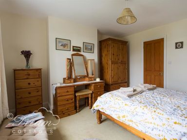 A bedroom with wooden furniture a bed a dressing table a tall chest of drawers and a wardrobe at Grazeland Cottage Bridport