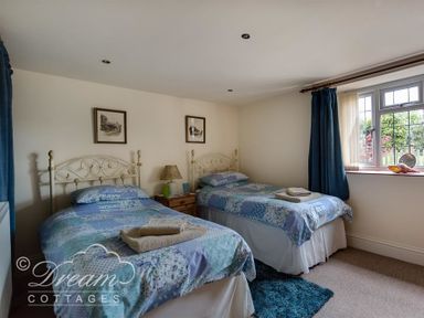 A bedroom with two single beds with patterned bedspreads a nightstand with a lamp and a window with blue curtains at Grazeland Cottage in Bridport
