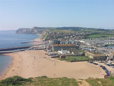 A beach with buildings and parked cars near the shore and hills in the background at Grazeland Cottage in Bridport