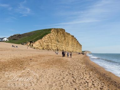A sandy beach with people walking near a large cliff and the ocean at Grazeland Cottage in Bridport