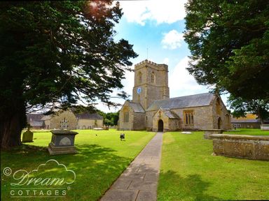 A stone church with a clock tower surrounded by grass and trees at Grazeland Cottage in Bridport