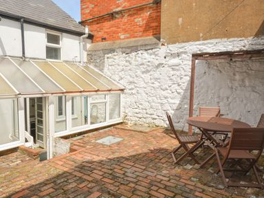 An outdoor patio with brick flooring a round table with four chairs and a white stone wall at Guinea Cottage Brewers Quay Harbour