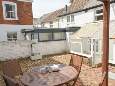 An outdoor patio area with a round table and chairs on brick flooring at Guinea Cottage in Brewers Quay Harbour
