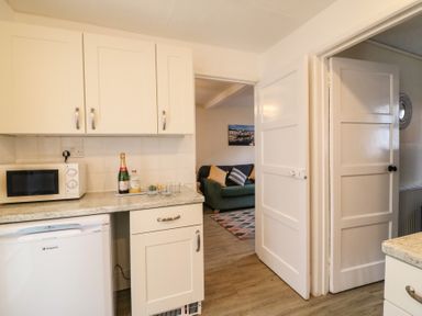 A kitchen with white cabinets microwave and fridge opening to a living room with sofa and cushions at Guinea Cottage in Brewers Quay Harbour