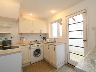 A kitchen with cabinets a washing machine a toaster knives a kettle and a sink next to a glass door at Guinea Cottage in Brewers Quay Harbour