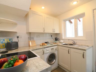 A kitchen with white cabinets a washing machine a sink and a bowl of fruit at Guinea Cottage in Brewers Quay Harbour