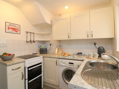A compact kitchen with white cabinets a stove washing machine and a sink at Guinea Cottage in Brewers Quay Harbour