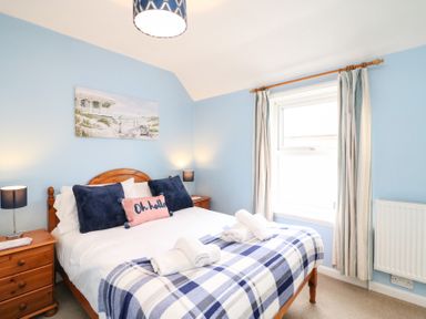A bedroom with a wooden bed frame blue walls and a window with curtains at Guinea Cottage Brewers Quay Harbour
