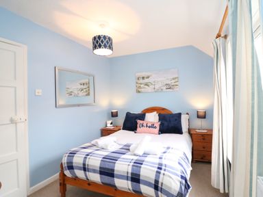 A bedroom with a double bed featuring blue and white checkered blanket and pillows with two wooden nightstands at Guinea Cottage Brewers Quay Harbour