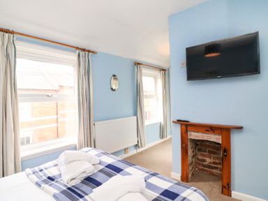 A bedroom with two windows and curtains a wall mounted television and a fireplace at Guinea Cottage in Brewers Quay Harbour