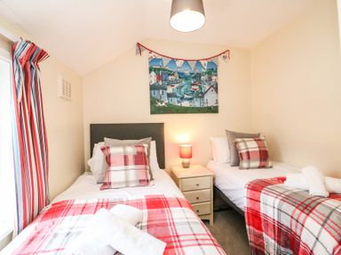 A bedroom with two single beds a nightstand with a lamp between them and red plaid bedding at Guinea Cottage in Brewers Quay Harbour