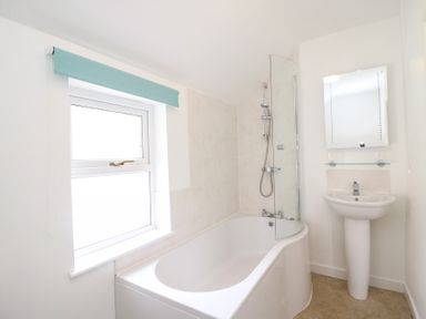A bathroom with a bathtub shower combo a window with a blue blind a pedestal sink and mirror at Guinea Cottage in Brewers Quay Harbour