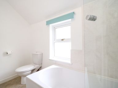A bathroom with a toilet a bathtub a window with a blue blind and a shower at Guinea Cottage in Brewers Quay Harbour