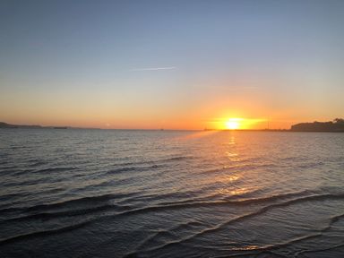 A sunset over the sea with gentle waves and ships on the horizon at Guinea Cottage in Brewers Quay Harbour