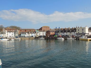 A harbor with boats docked by buildings and cars parked along the waterfront at Brewers Quay Harbour