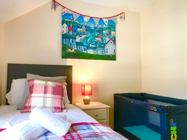 A bedroom with a single bed side table lamp and a playpen at Guinea Cottage Brewers Quay Harbour