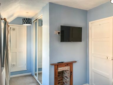 A room with blue walls a wall mounted television a small fireplace a white door mirrored closet doors and a hanging ceiling lamp at Guinea Cottage Brewers Quay Harbour