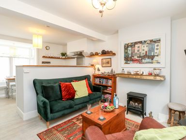 A living room with a green sofa, wooden coffee table, shelves with books and decorations, and a painting above a small stove at Harbour Catch Cottage in Weymouth
