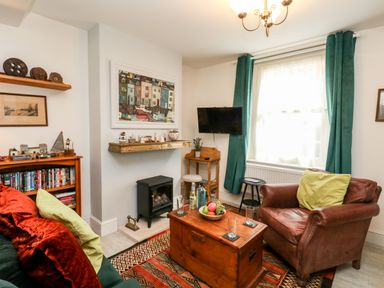 A living room with a leather armchair green curtains a wooden chest as a coffee table and a wall mounted tv at Harbour Catch Cottage in Weymouth