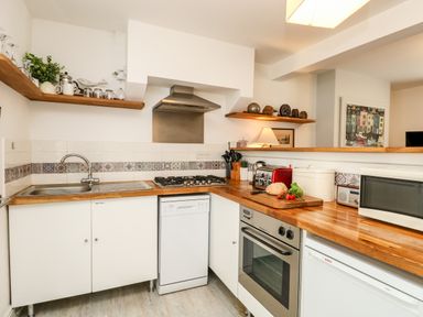 A kitchen with wooden countertops a sink stove oven microwave open shelves and kitchen utensils at Harbour Catch Cottage in Weymouth