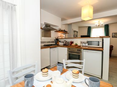 A kitchen with an oven dishwasher microwave and countertop with cups muffins and a teapot at Harbour Catch Cottage in Weymouth