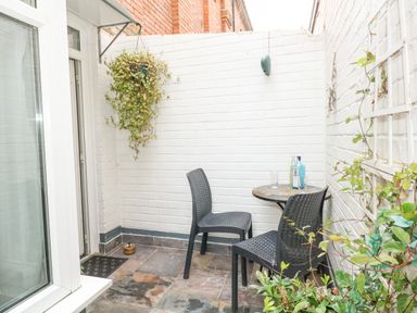 A small outdoor patio with two black chairs a round table with bottles and glasses and plants on a wall at Harbour Catch Cottage in Weymouth