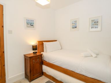 A single bed with white bedding and rolled towels on top next to a wooden nightstand with a lamp in a bedroom at Harbour Catch Cottage in Weymouth