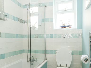 A bathroom with a bathtub shower combo a toilet and a window with a decorative boat at Harbour Catch Cottage in Weymouth