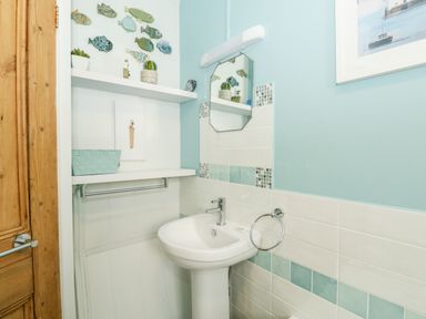 A bathroom with a pedestal sink mirror towel ring shelves with decorations and a wooden door at Harbour Catch Cottage in Weymouth