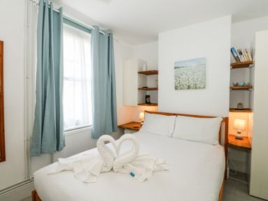 A bedroom with a double bed and folded towel swans next to a window with blue curtains at Harbour Catch Cottage in Weymouth