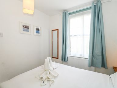A bedroom with a bed and towels folded on it next to a window with blue curtains at Harbour Catch Cottage in Weymouth