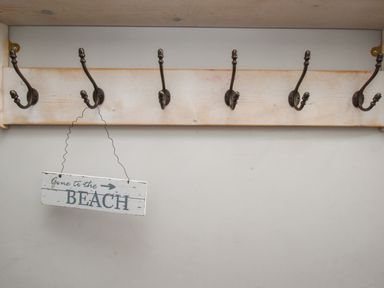 A wooden coat rack with six metal hooks and a sign hanging that reads gone to the beach at Harbourside House Brewers Quay Harbour