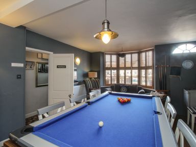 A game room with a blue pool table chairs a sofa striped armchair and windows with shutters at Harbourside House in Brewers Quay Harbour