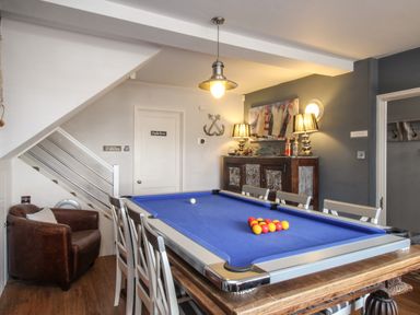 A room with a blue pool table surrounded by chairs a brown armchair under stairs a cabinet with lamps and decorative items and a door labeled engine room at Harbourside House Brewers Quay Harbour