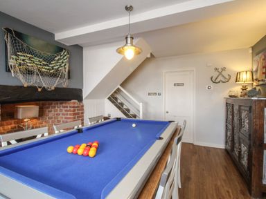 A game room with a blue pool table chairs wooden cabinet and wall decorations at Harbourside House in Brewers Quay Harbour