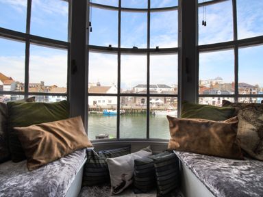 A window seat with cushions overlooking boats and buildings across the water at Harbourside House in Brewers Quay Harbour