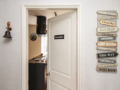A door labeled Quartermaster opens to a kitchen with a counter and black range hood with decorative signs on the wall at Harbourside House in Brewers Quay Harbour