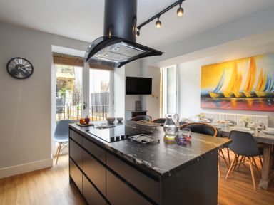 A kitchen island with a cooktop and a dining table with chairs and a painting of sailboats on the wall at Harbourside House in Brewers Quay Harbour