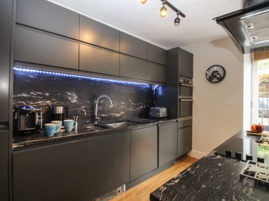 A kitchen with black cabinets a coffee maker toaster and a wall clock at Harbourside House in Brewers Quay Harbour