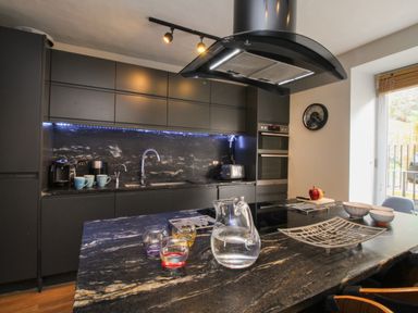 A kitchen with dark cabinets a marble countertop a glass pitcher and mugs at Harbourside House in Brewers Quay Harbour