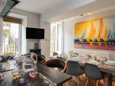 A dining room with a table set for a meal chairs a TV on the wall and a painting of sailboats at Harbourside House Brewers Quay Harbour
