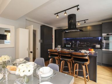 A kitchen and dining area with a glass dining table set with plates and glasses and a kitchen island with bar stools at Harbourside House in Brewers Quay Harbour