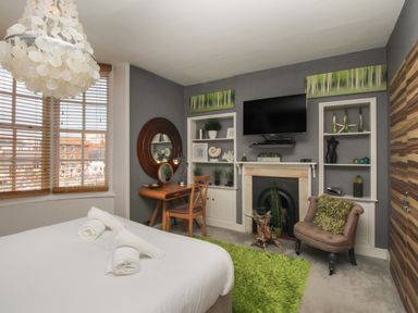 A bedroom with a bed with rolled towels a desk with a chair a wall mounted television and a green rug at Harbourside House Brewers Quay Harbour