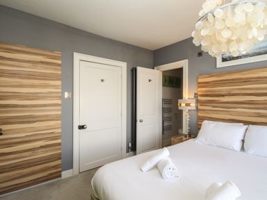 A bedroom with a bed with white sheets and towels a wooden headboard grey walls and white doors at Harbourside House in Brewers Quay Harbour