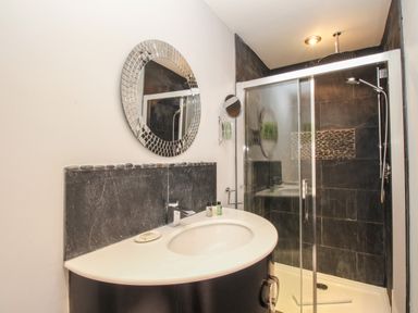 A bathroom with a sink counter and a round mirror next to a glass shower enclosure at Harbourside House in Brewers Quay Harbour
